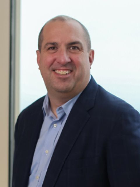 Man in a blue blazer and button-down shirt smiling, likely in an office setting.