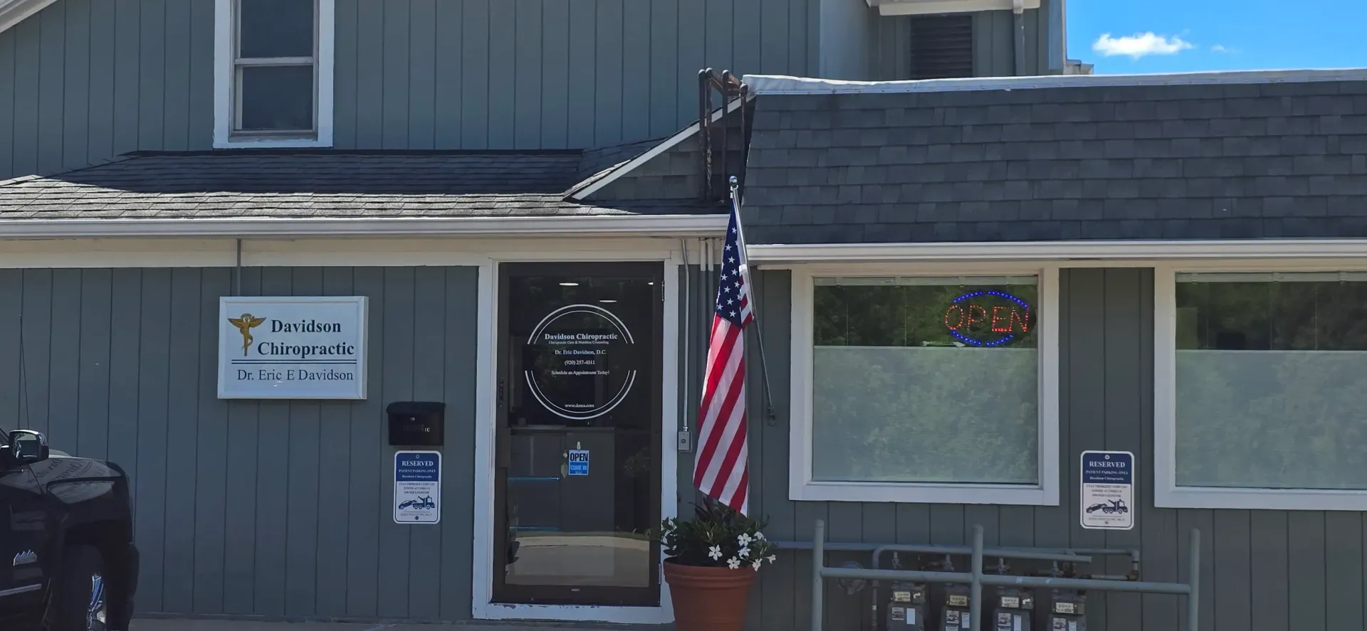 Gray building entrance with a sign, American flag, and a window beside a door with a wreath