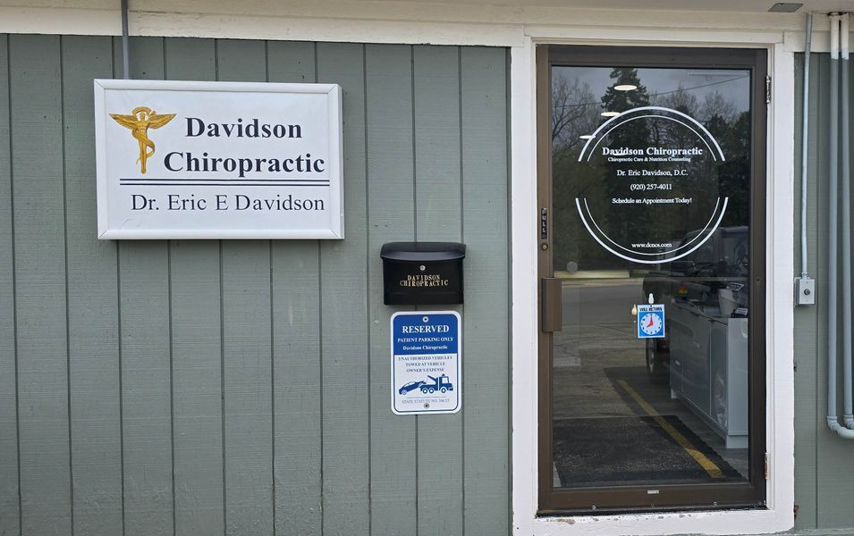 Entrance to a chiropractic office with a sign and glass door on a gray exterior wall