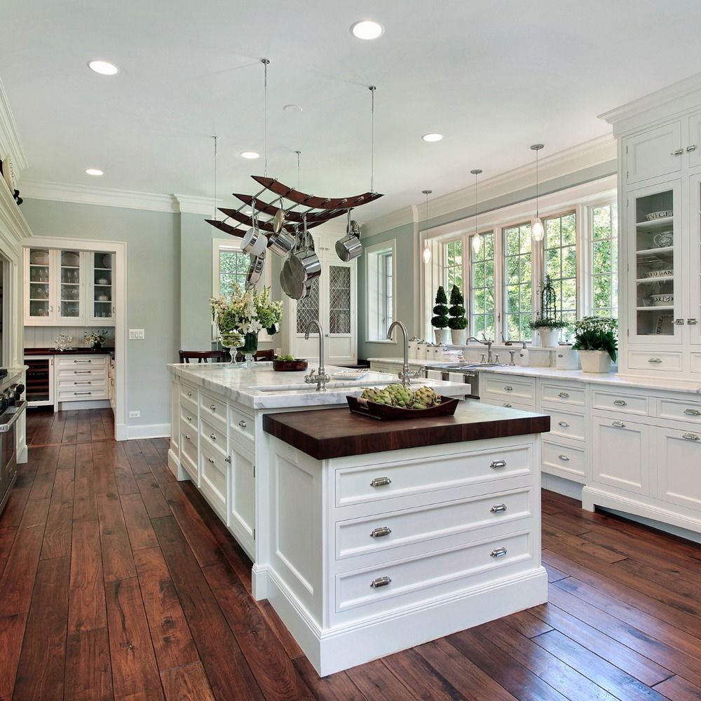 Elegant white kitchen with island, wood floor, and large windows.