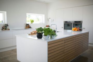 Modern kitchen with white countertops, wooden island, herbs, and fruit.