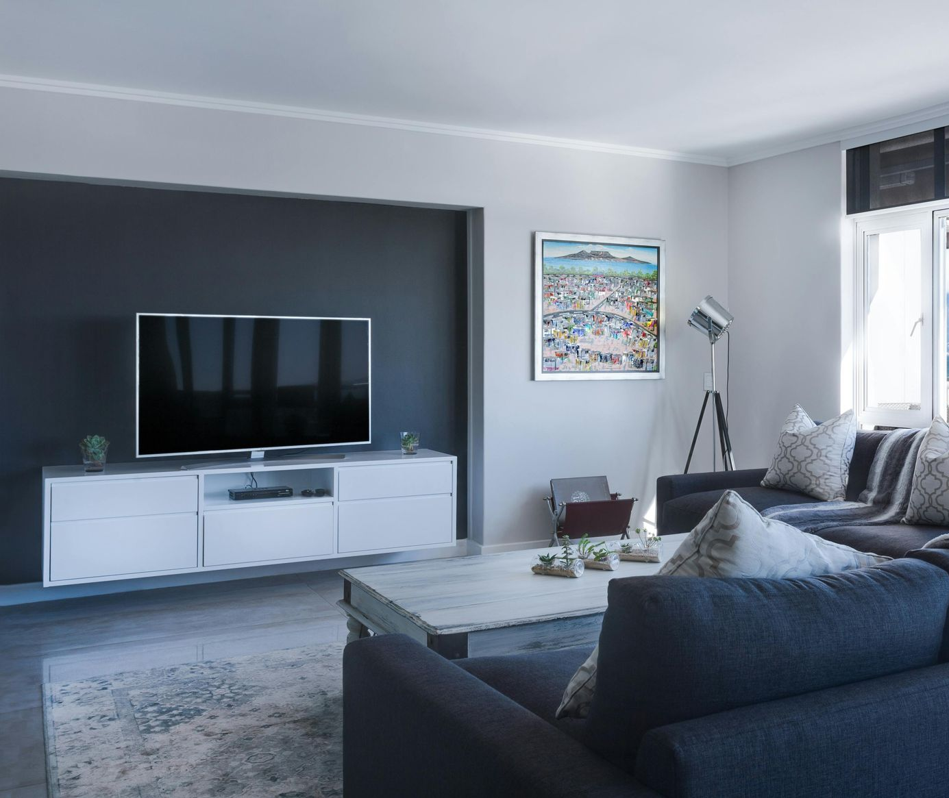 Living room with a large TV on a dark accent wall, gray sofa, and modern decor.