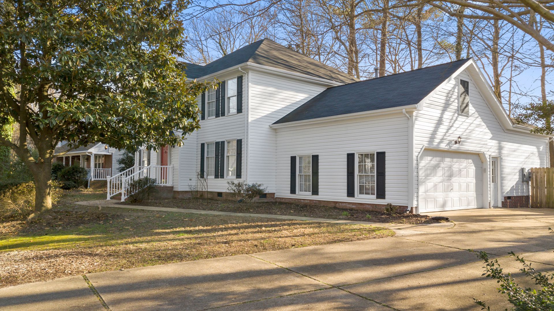 White two-story house with black shutters, attached garage, and a large tree in front.