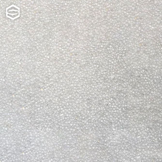 Primo piano di una superficie ricoperta da numerose piccole particelle granulari bianche, che appaiono leggermente ruvide.