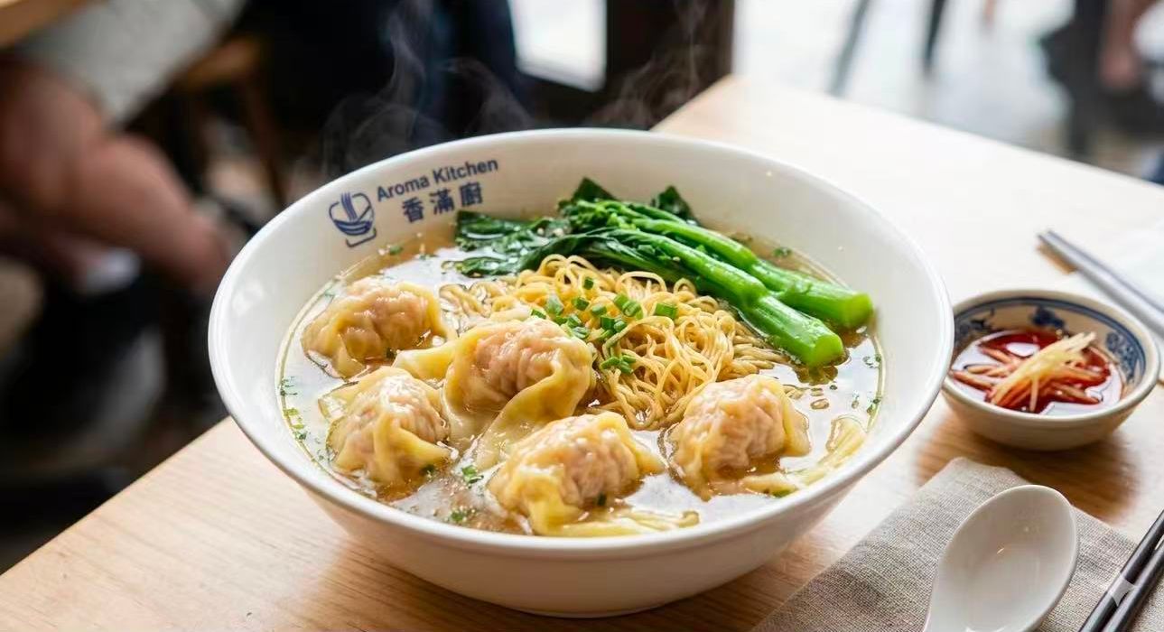 Bowl of dumpling noodle soup topped with green vegetables on a restaurant table