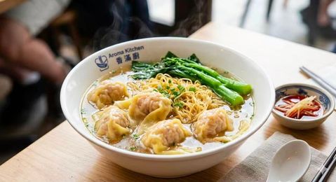 Bowl of dumpling noodle soup topped with green vegetables on a restaurant table