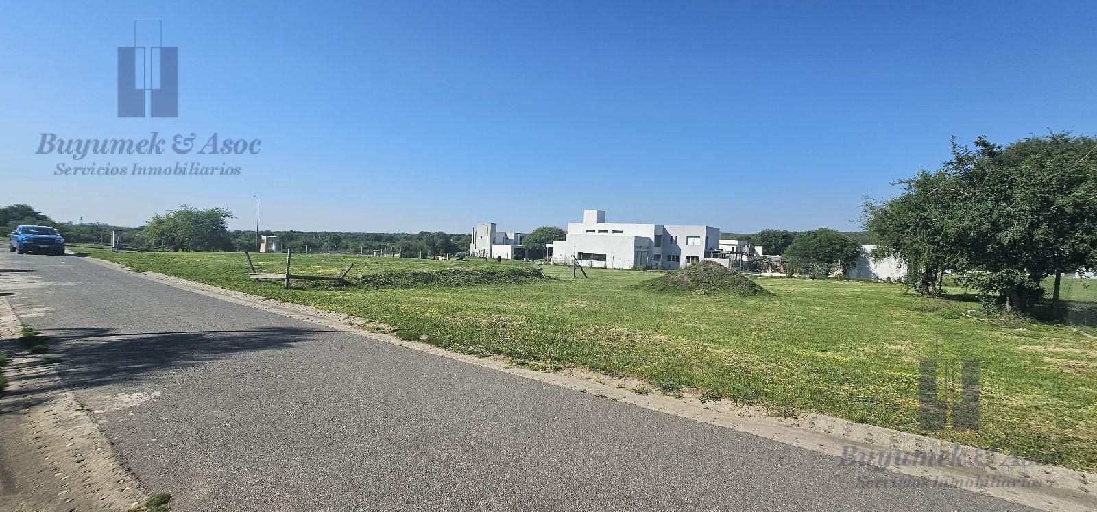 Campo de hierba bajo un cielo azul despejado con una carretera y edificios lejanos en el horizonte.