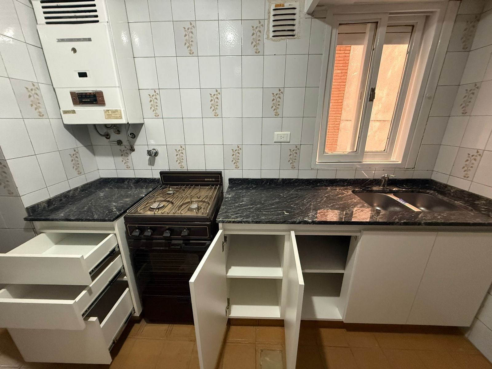 Habitación vacía con suelo de madera brillante, paredes blancas, luces en el techo y una ventana al fondo.