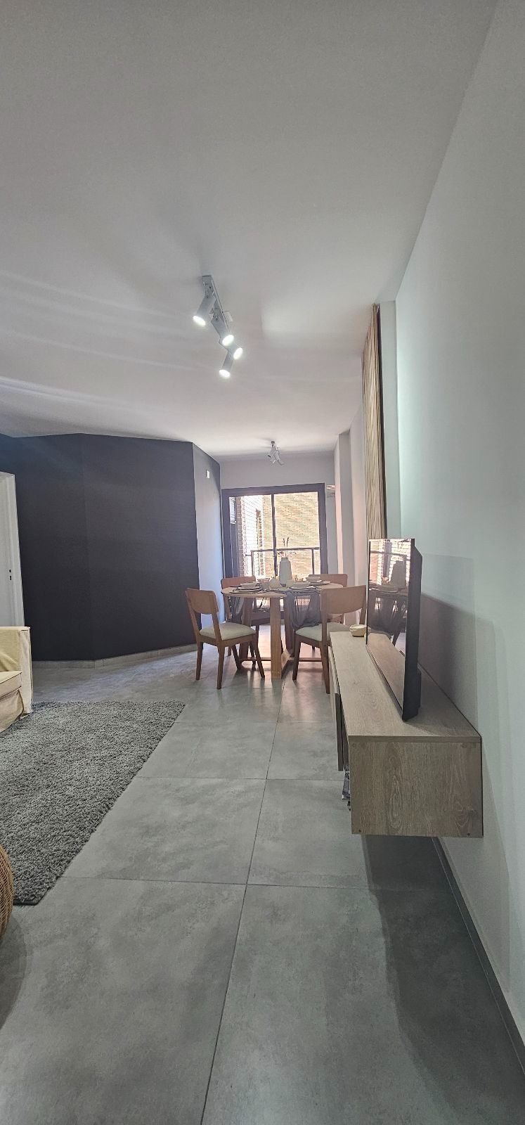 Comedor moderno con una mesa redonda de madera, sillas naranjas y una pared decorativa oscura.