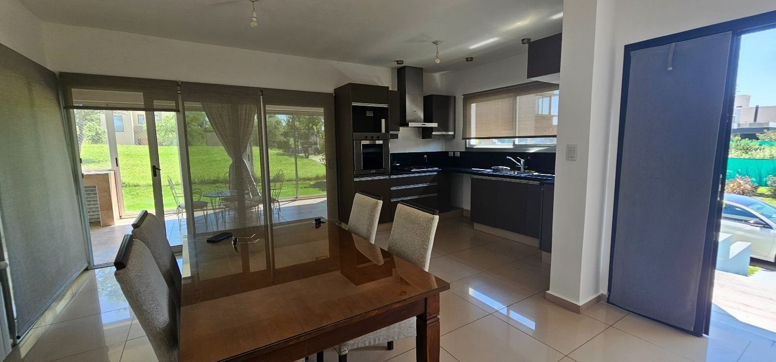 Comedor y cocina amplios y luminosos con puertas de cristal, mesa de madera y vistas a una piscina exterior.