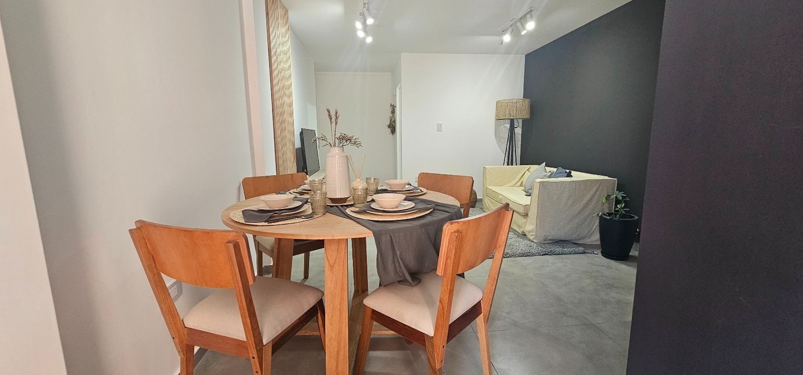 Comedor moderno con una mesa redonda de madera, sillas naranjas y una pared decorativa oscura.