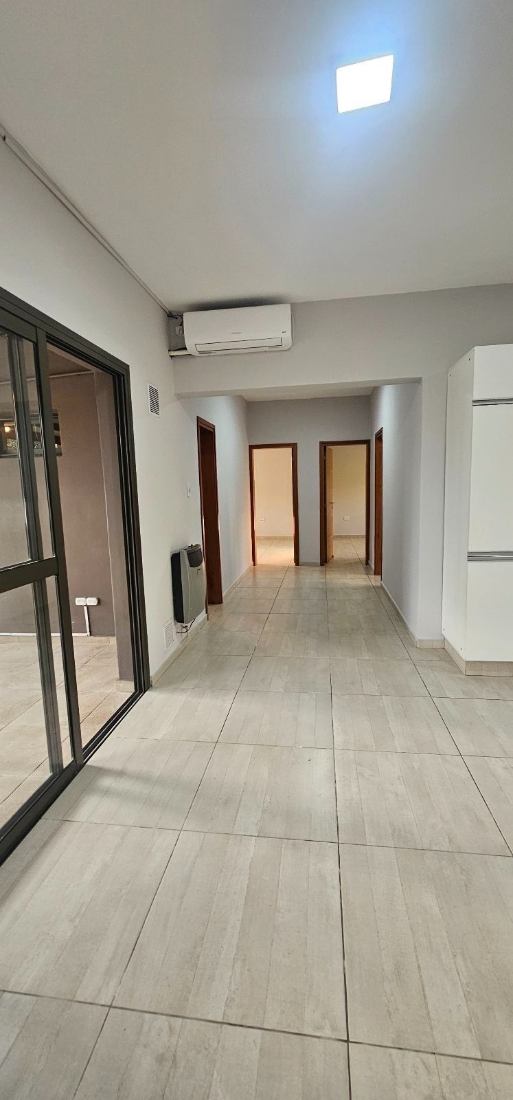 Cocina moderna vacía con gabinetes blancos, encimeras negras y piso de baldosas claras bajo iluminación empotrada.