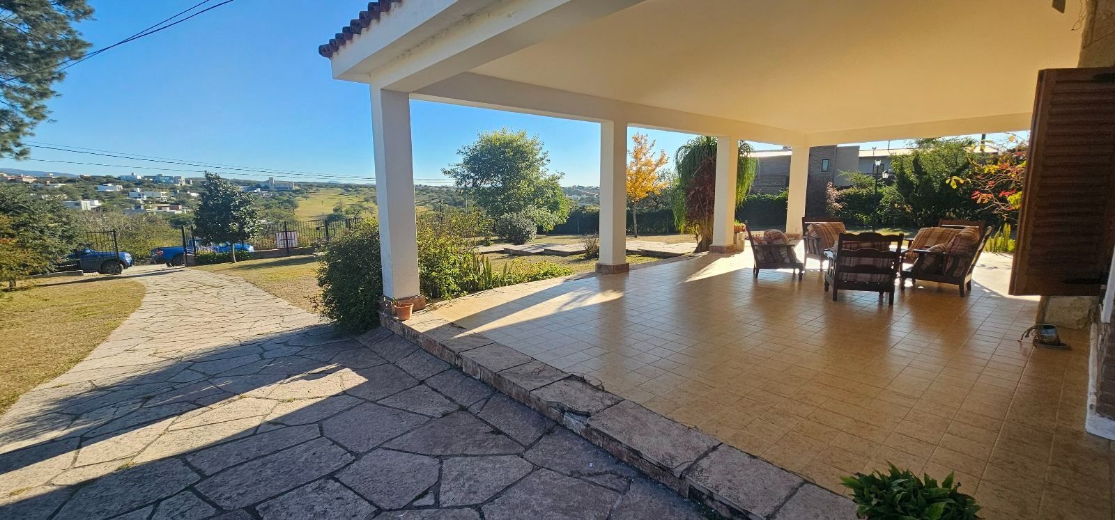 Casa de una sola planta con porche delantero, amplio césped y entrada para vehículos bajo un cielo azul despejado.