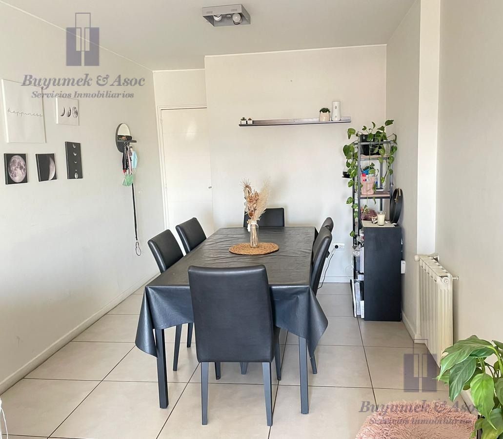 Comedor con mesa y sillas negras, paredes blancas, decoración en las paredes y una estantería alta para plantas.