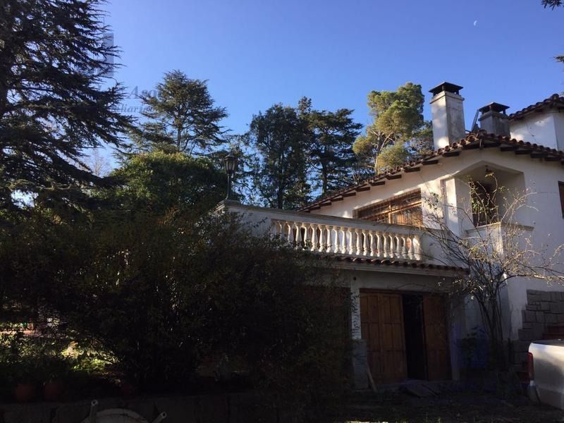 Casa soleada de estilo mediterráneo con balcón, árboles altos y cielo azul.