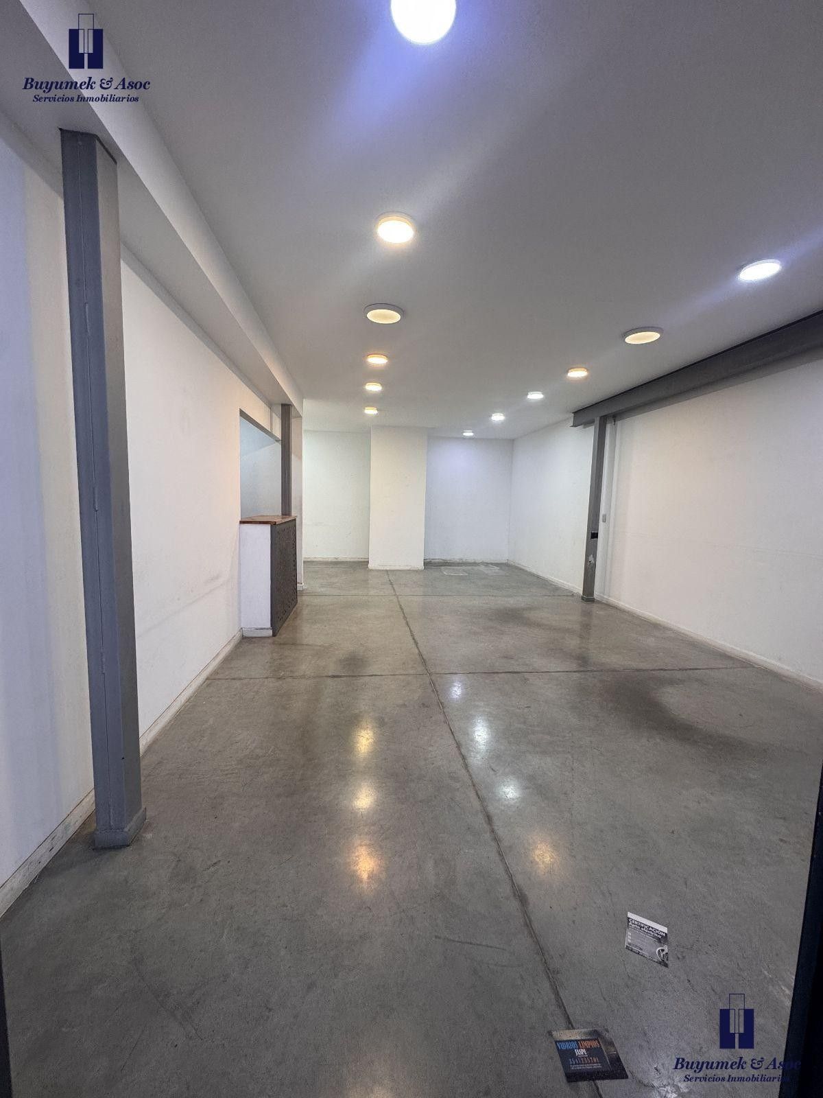Vestíbulo moderno y vacío con suelo de hormigón pulido, luces empotradas y puertas de cristal al fondo.
