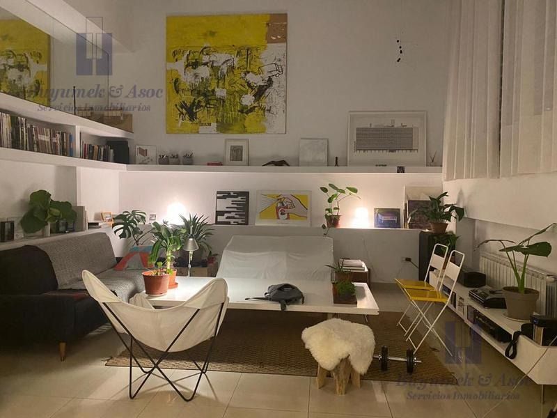 Acogedora sala de estar con estantes blancos, plantas, obras de arte amarillas y un sofá y una silla oscuros junto a la chimenea.