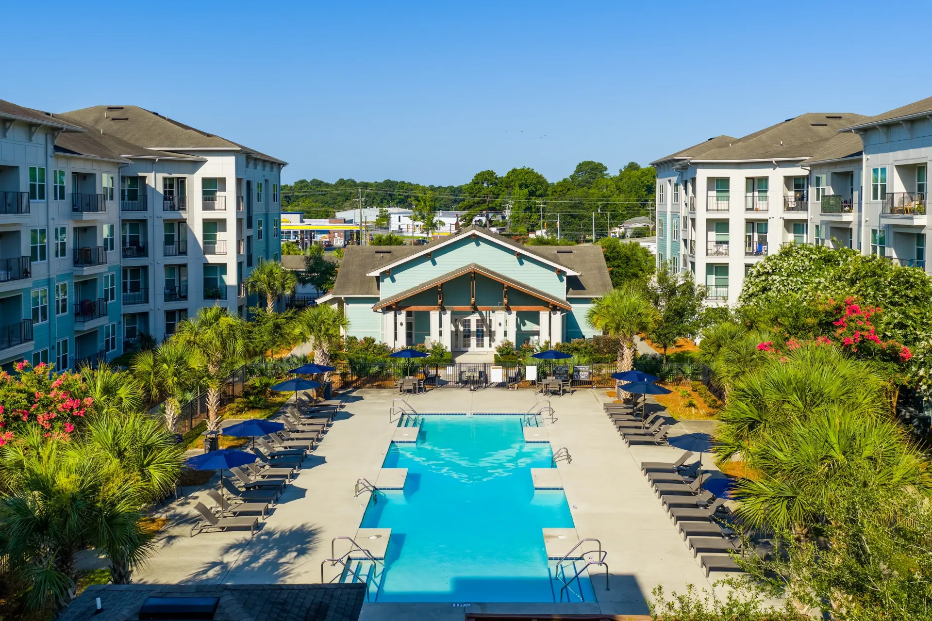 Outdoor swimming pool area with lounge chairs and umbrellas, surrounded by apartment buildings at Atlantic on the Avenue in North Charleston, SC.