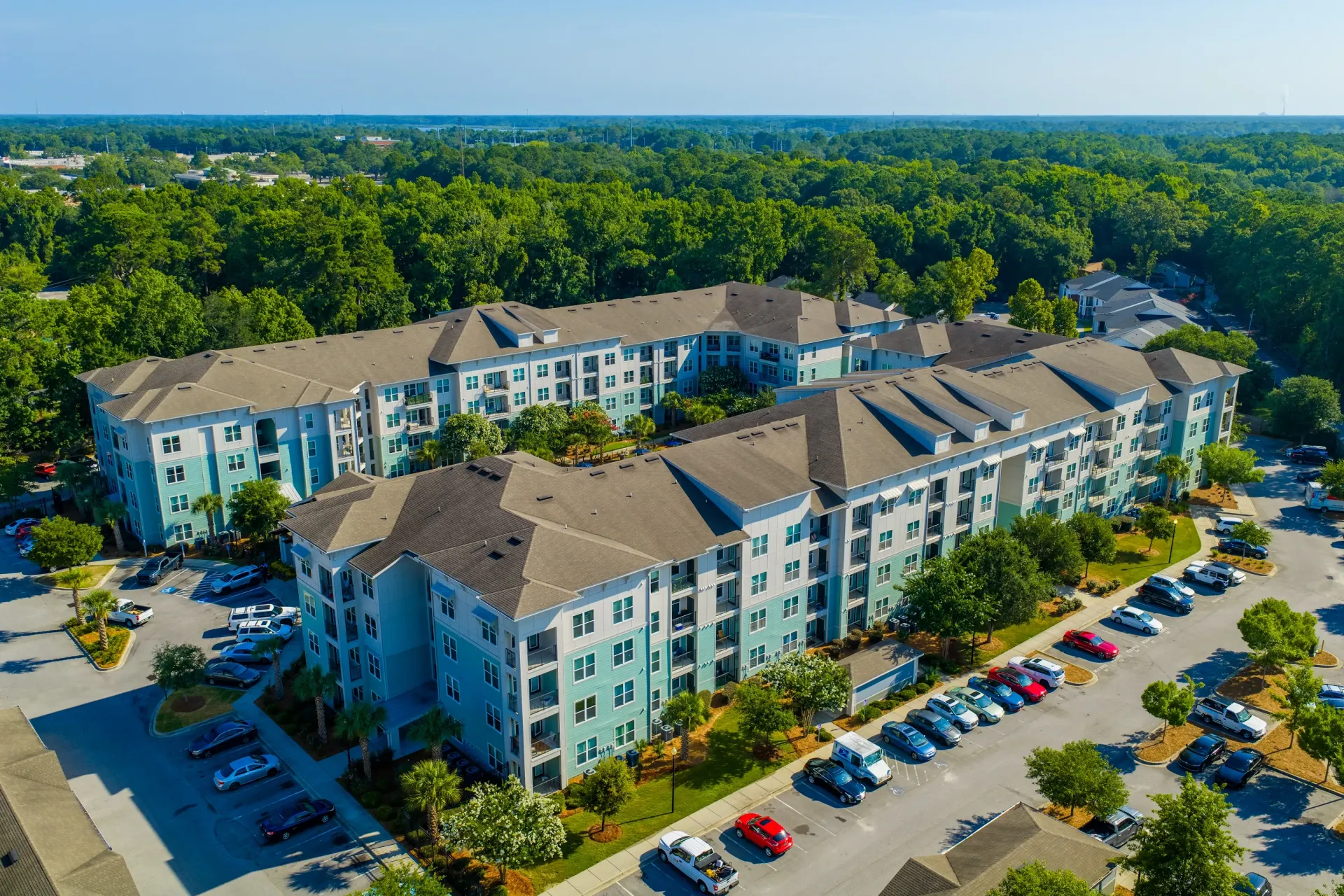 Aerial view of a large apartment building exterior with a parking lot and trees at Atlantic on the Avenue in North Charleston, SC.