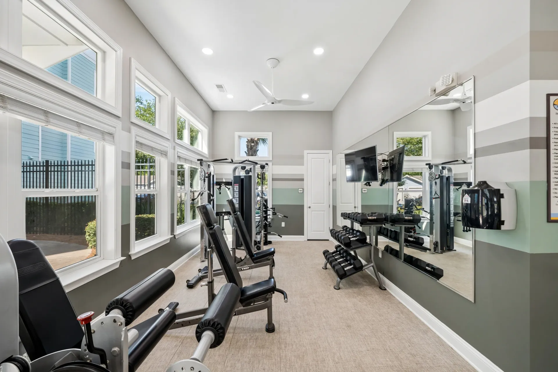 Gym equipment including weight machines and dumbbells, with mirrors on the wall.