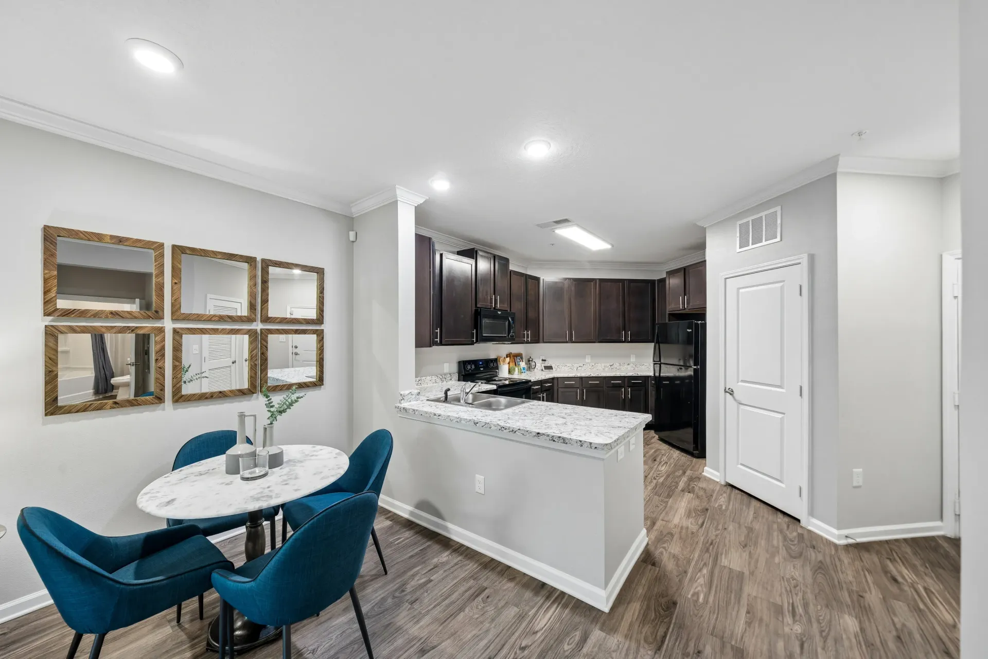 Modern kitchen and dining area with granite countertops, dark wood cabinets, and blue chairs at Atlantic on the Avenue in North Charleston, SC.