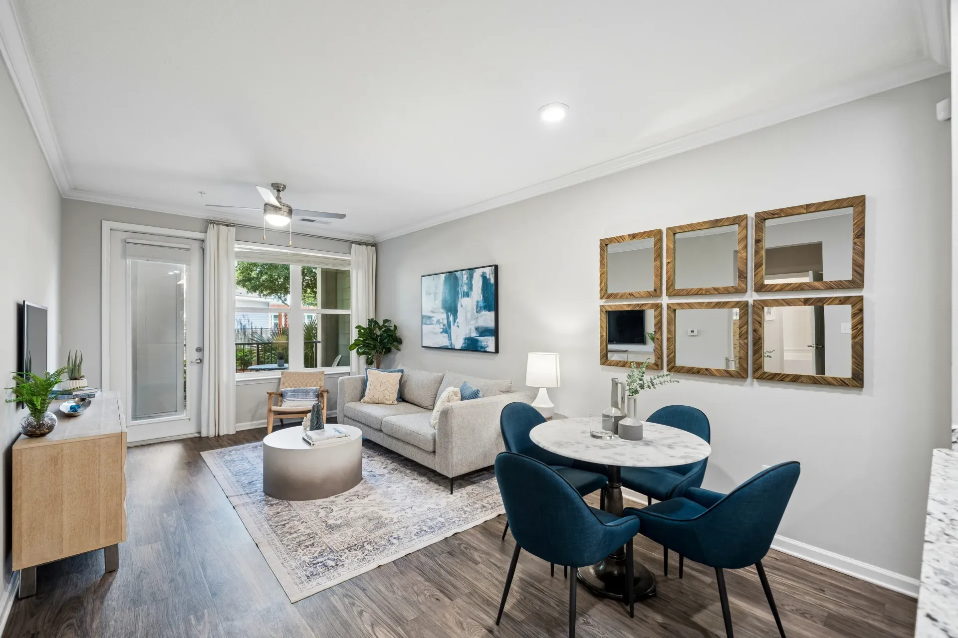 Modern living and dining area with gray sofa, blue chairs, and marble table.