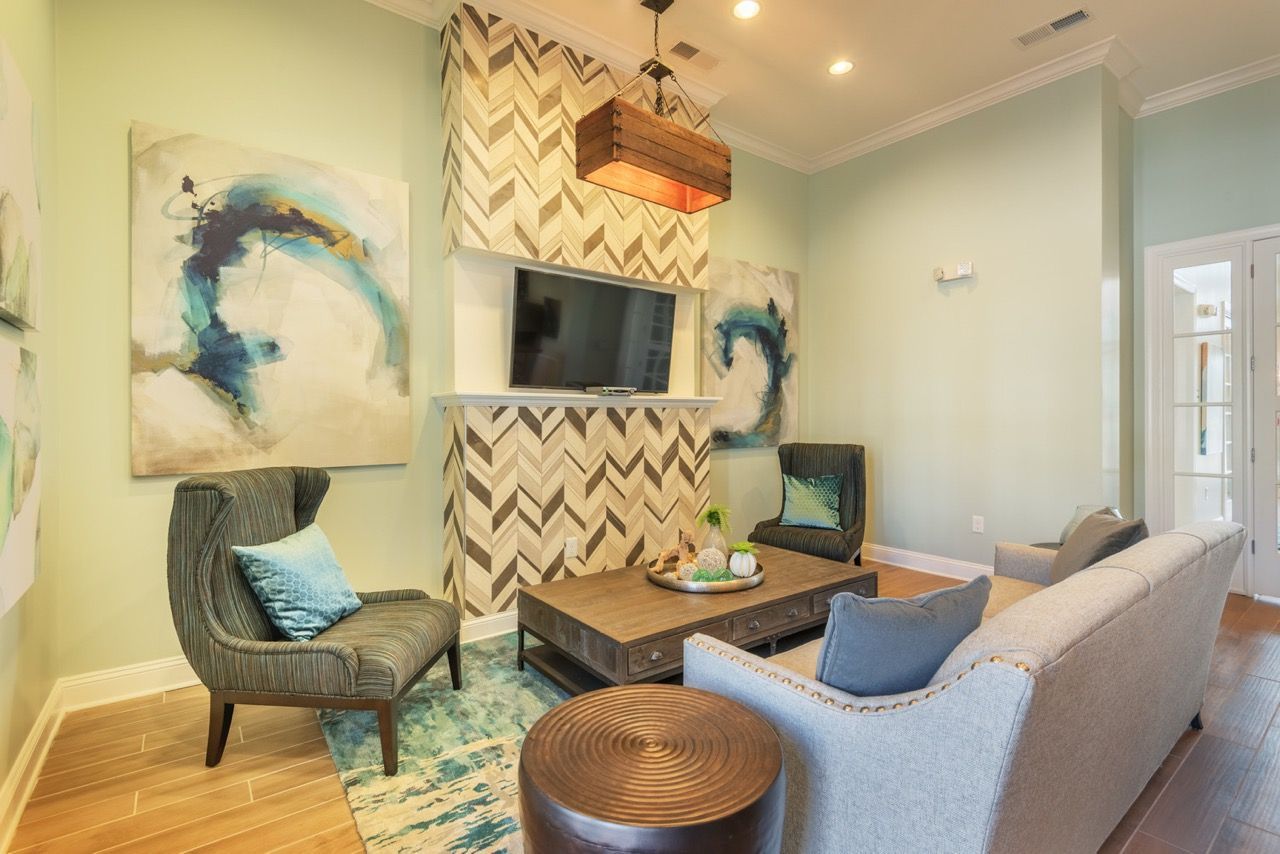 Living room in a modern apartment with mint green walls, gray sofa, teal chairs, and a wall-mounted TV at Atlantic on the Avenue in North Charleston, SC.