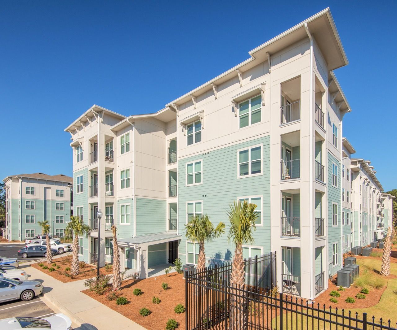 Exterior view of a modern apartment building with balconies and palm trees against a blue sky at Atlantic on the Avenue in North Charleston, SC.