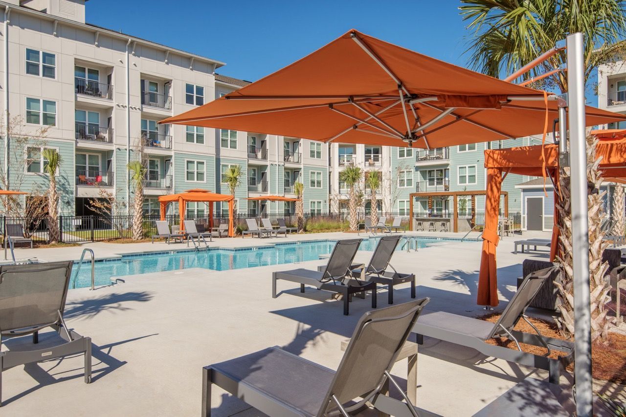 Outdoor pool area with lounge chairs and orange shade umbrellas at a modern apartment community at Atlantic on the Avenue in North Charleston, SC.