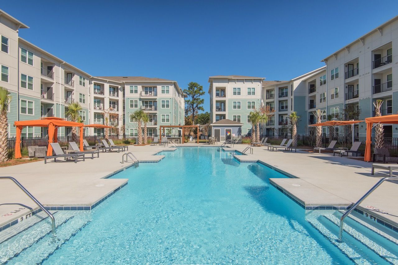 Outdoor community swimming pool bordered by apartment buildings, lounge chairs, and orange cabanas at Atlantic on the Avenue in North Charleston, SC.