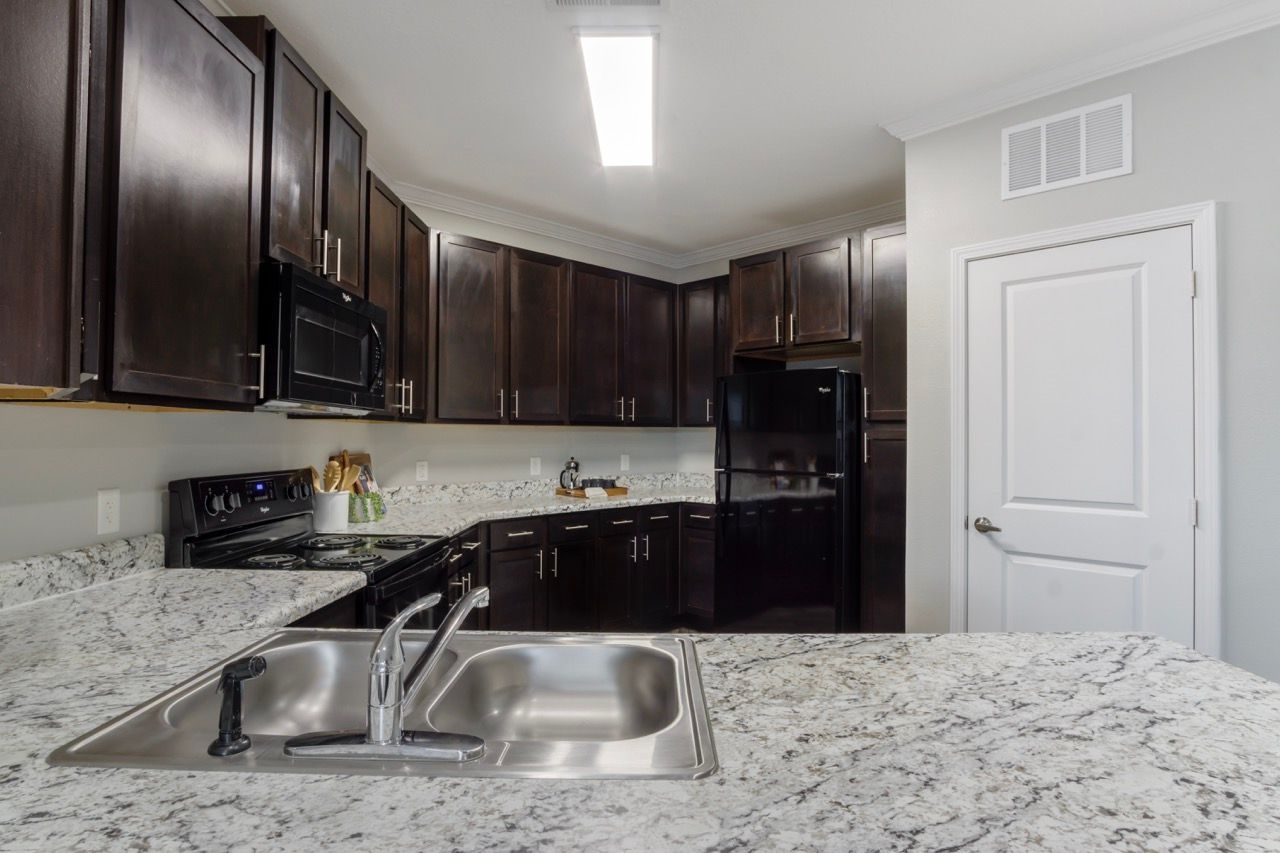 Kitchen with dark wood cabinets, granite countertops, and stainless steel appliances at Atlantic on the Avenue in North Charleston, SC.