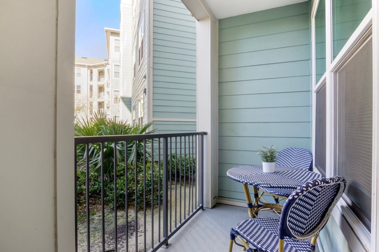 Balcony with blue-green siding, metal railing, and a small round table with two chairs at Atlantic on the Avenue in North Charleston, SC.