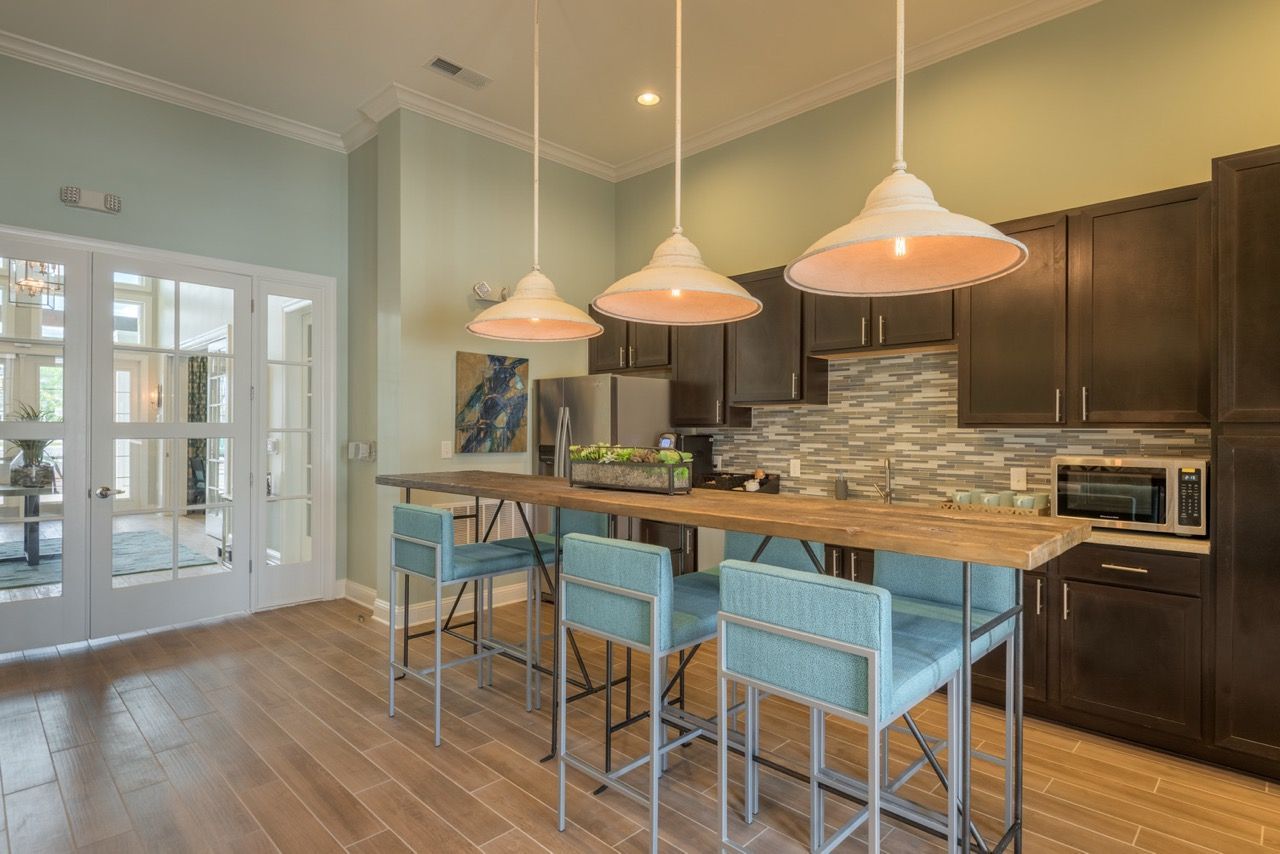 Open-concept kitchen with a wooden island, blue bar stools, pendant lights, and stainless steel appliances at Atlantic on the Avenue in North Charleston, SC.