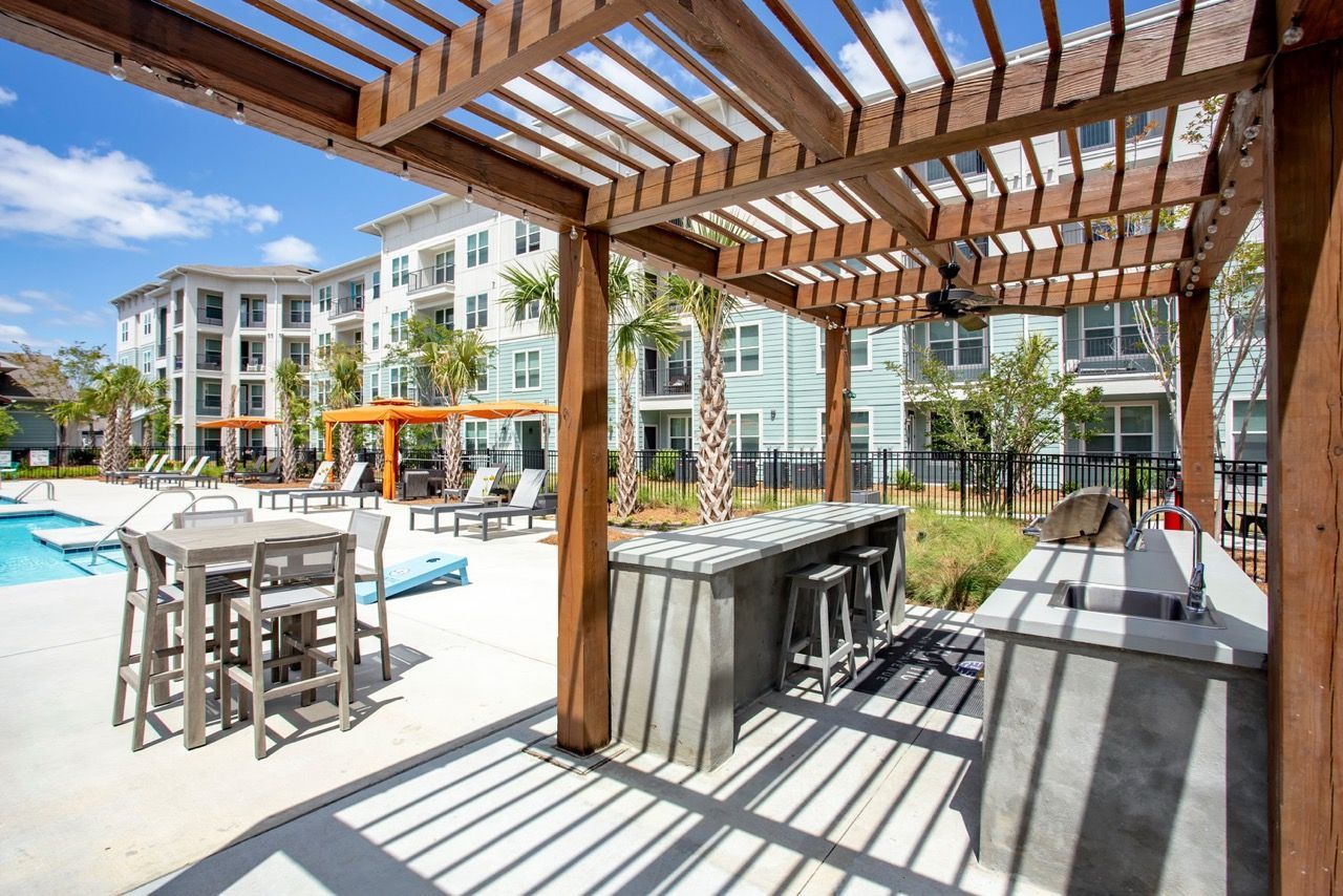 Outdoor pool area with lounge chairs, tables, and a wooden pergola at Atlantic on the Avenue in North Charleston, SC.