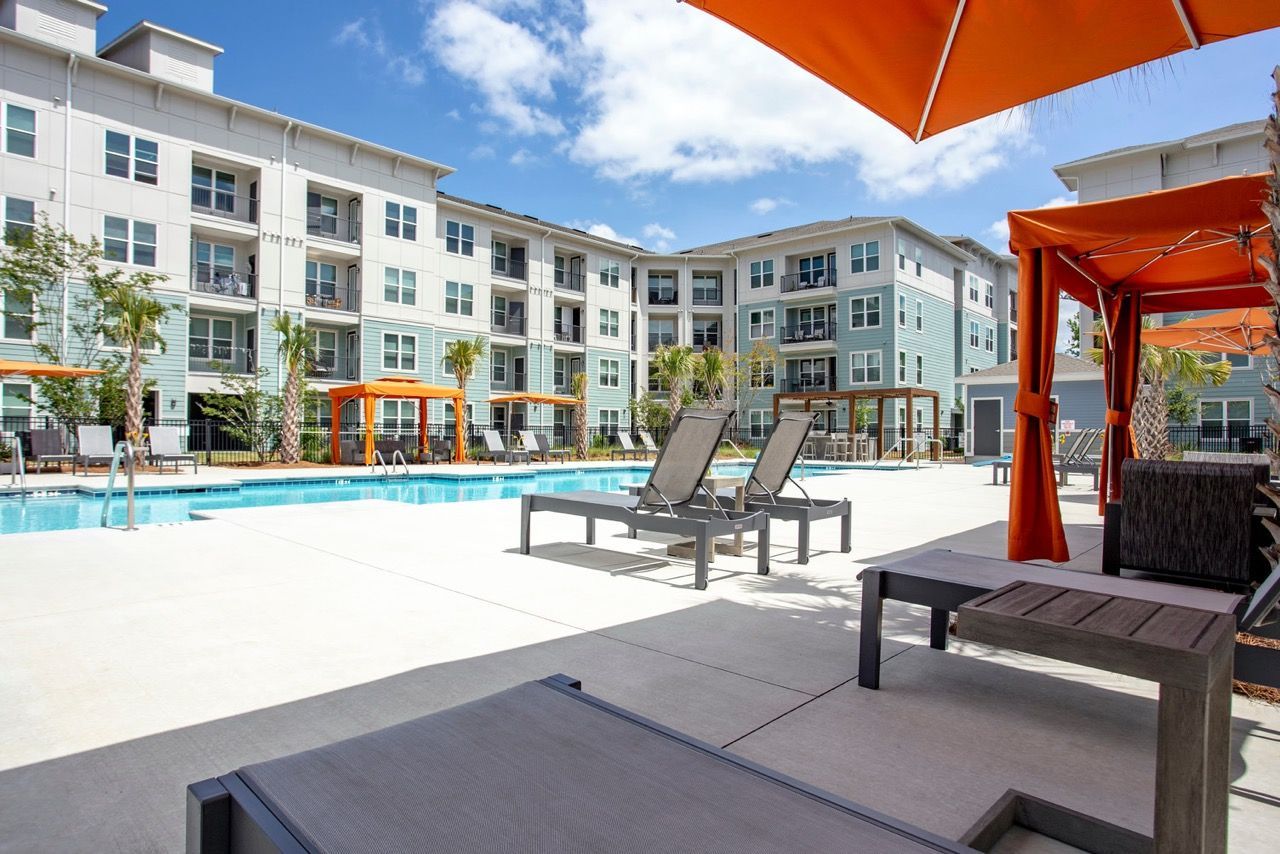 Outdoor pool area with lounge chairs and orange cabanas at a modern apartment complex at Atlantic on the Avenue in North Charleston, SC.
