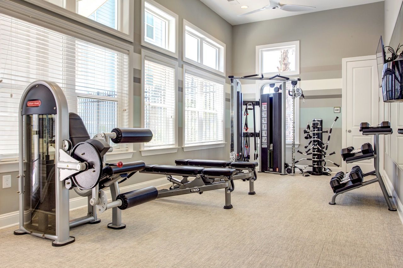 Bright community gym with weight machines, a bench, and free weights at Atlantic on the Avenue in North Charleston, SC.