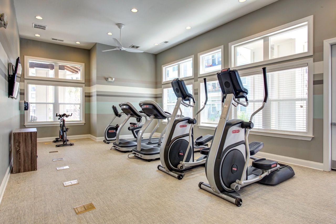 Indoor community gym with multiple cardio machines and large windows at Atlantic on the Avenue in North Charleston, SC.