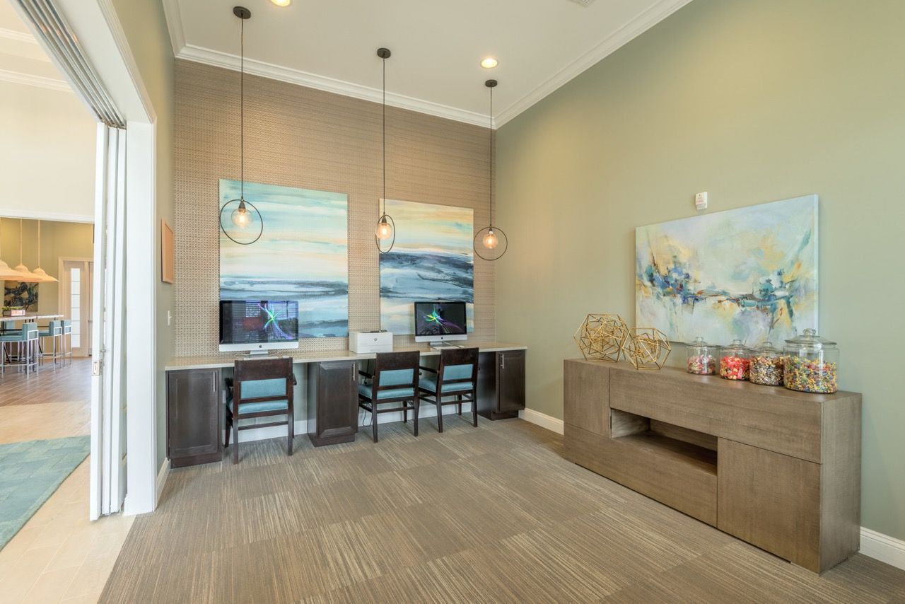 Community lounge with built-in desks, computer stations, pendant lights, and artwork at Atlantic on the Avenue in North Charleston, SC.