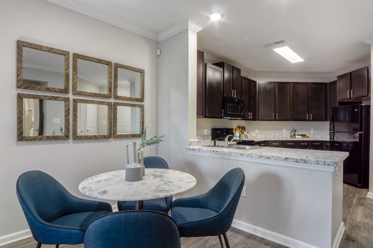 Open dining area with a round marble table and blue chairs next to a granite-counter kitchen at Atlantic on the Avenue in North Charleston, SC.