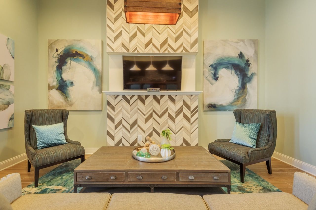 Common area lounge with two striped chairs, a coffee table, abstract art, and TV above a chevron fireplace at Atlantic on the Avenue in North Charleston, SC.