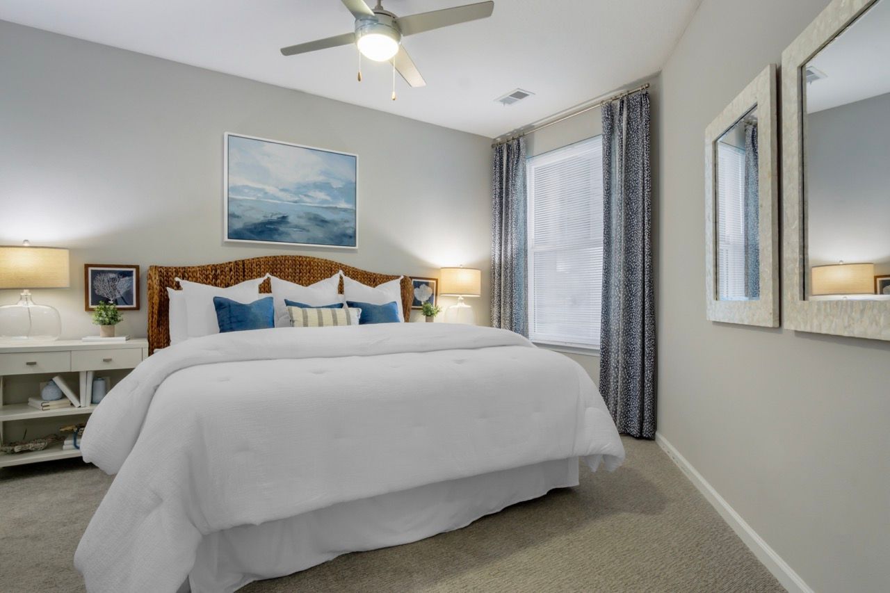 Bedroom in an apartment with a large bed, two nightstands, and windows with curtains at Atlantic on the Avenue in North Charleston, SC.