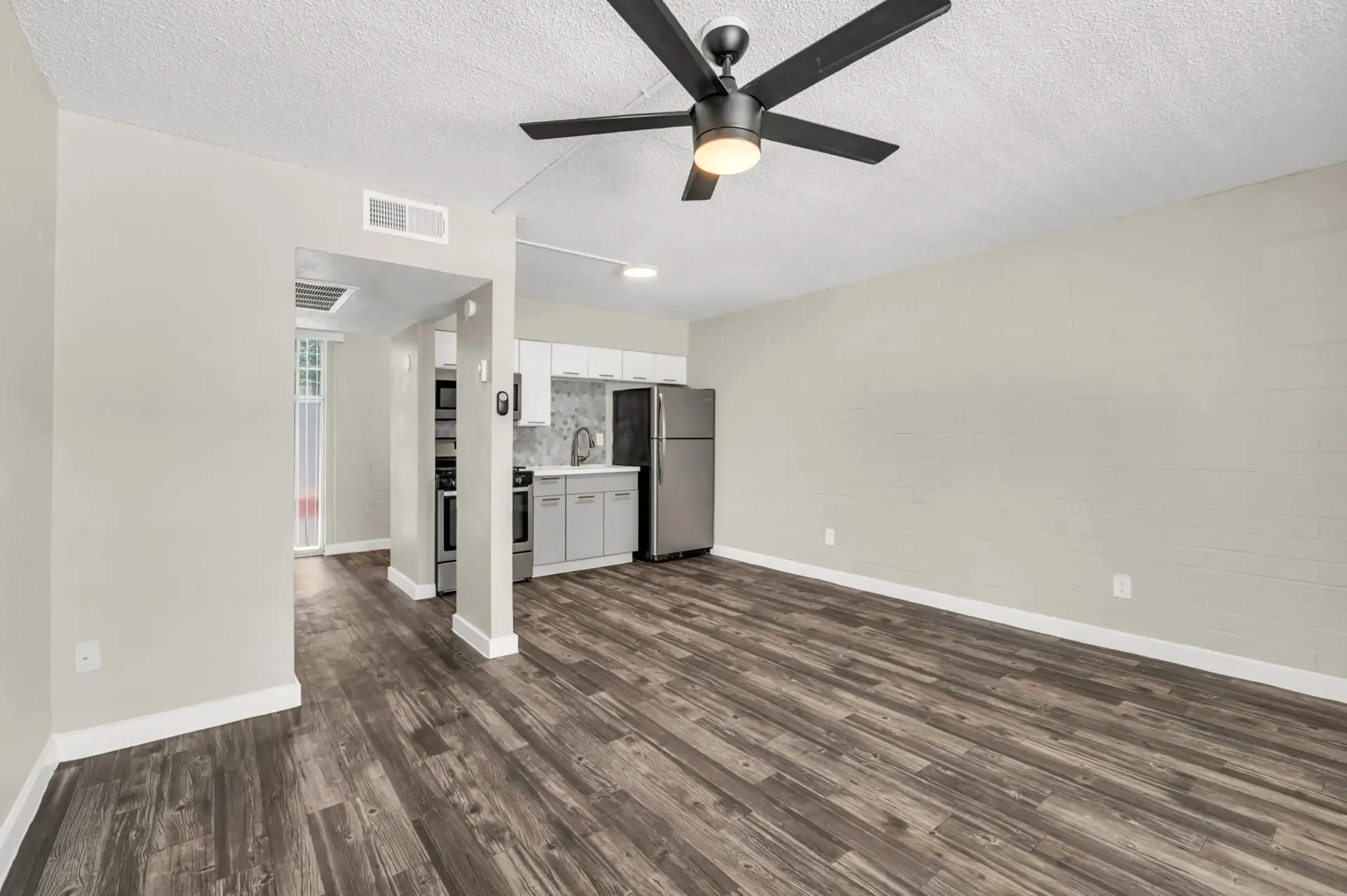 a living room with a ceiling fan and a kitchen in the background