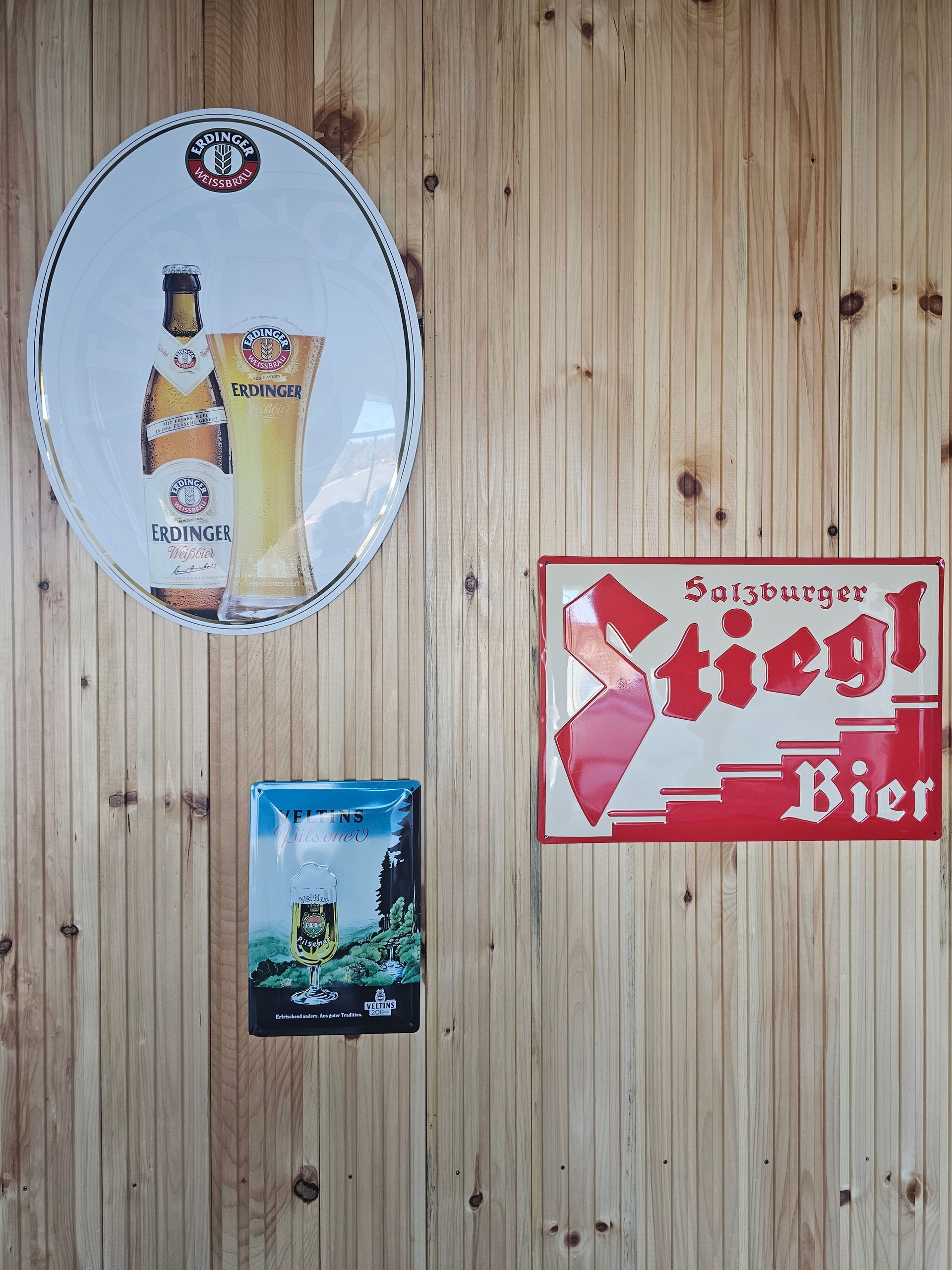 Three beer signs on a wooden wall: oval with bottle & glass, rectangular with 
