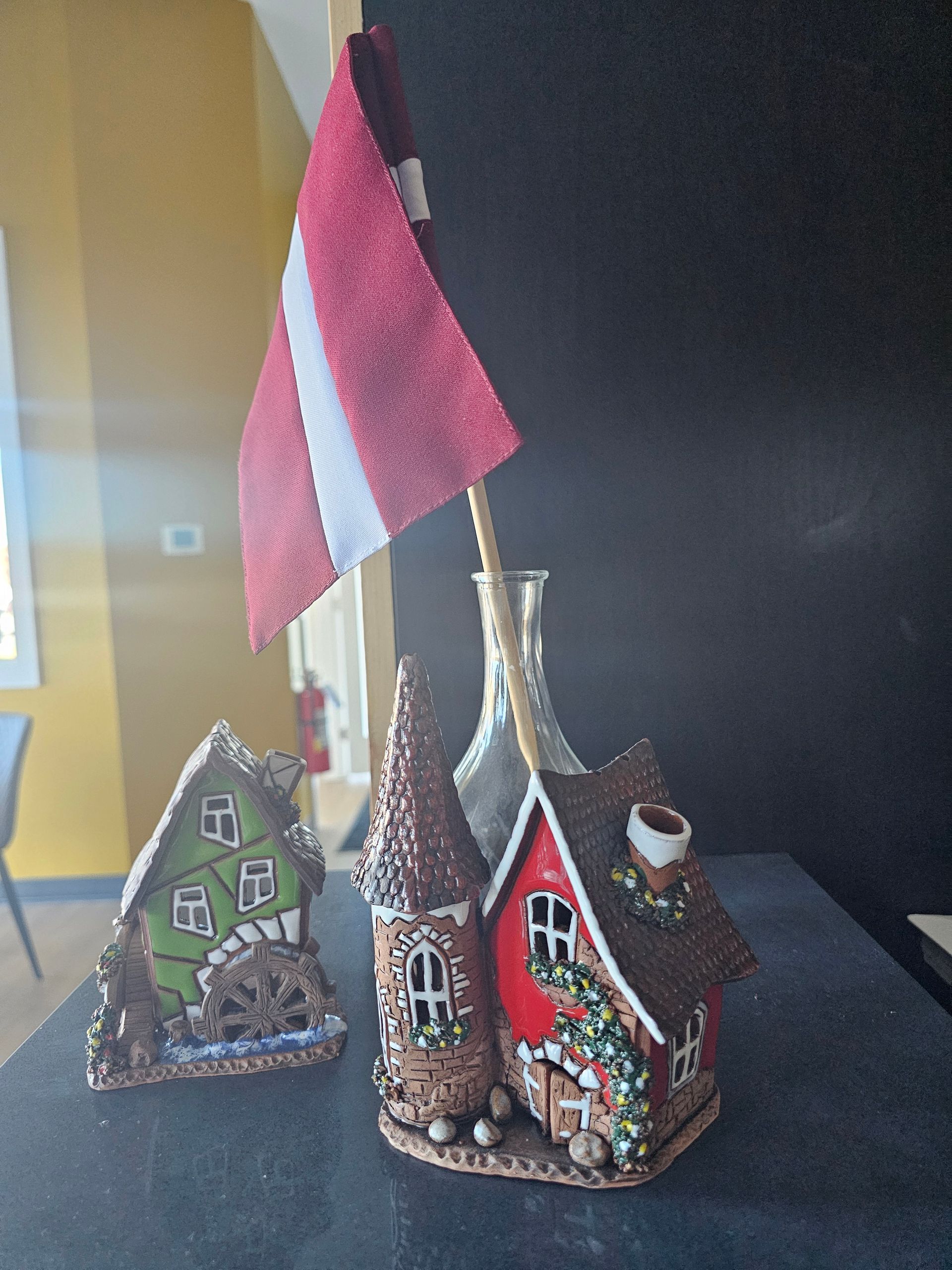 Three gingerbread houses with a Latvian flag on a table. One is green, the other two are brown with red and white accents.