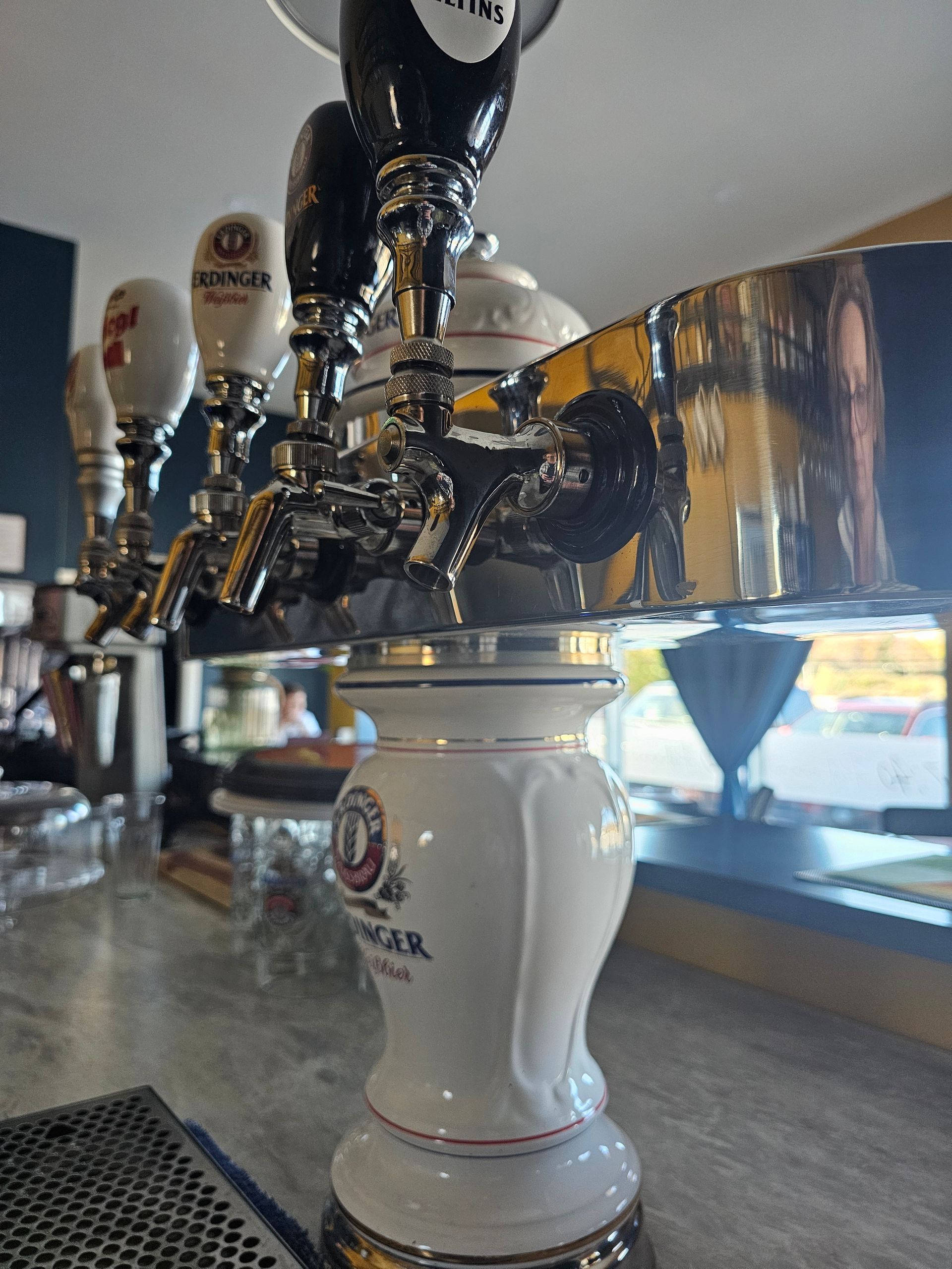 Close-up of a beer tap tower with multiple taps on a bar. White ceramic base, silver fixtures.