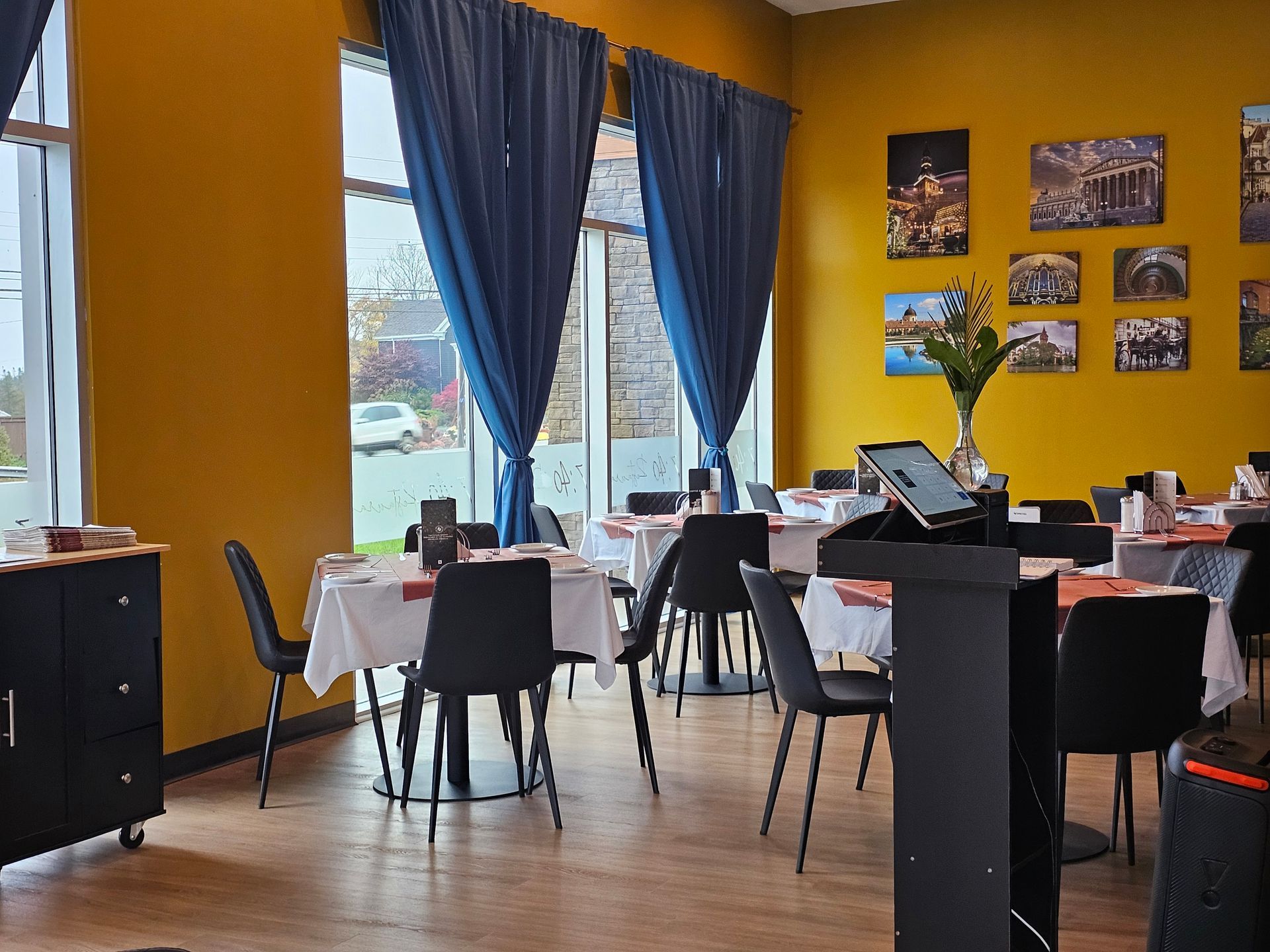 Restaurant interior with yellow walls, tables with white tablecloths, black chairs, and blue curtains.