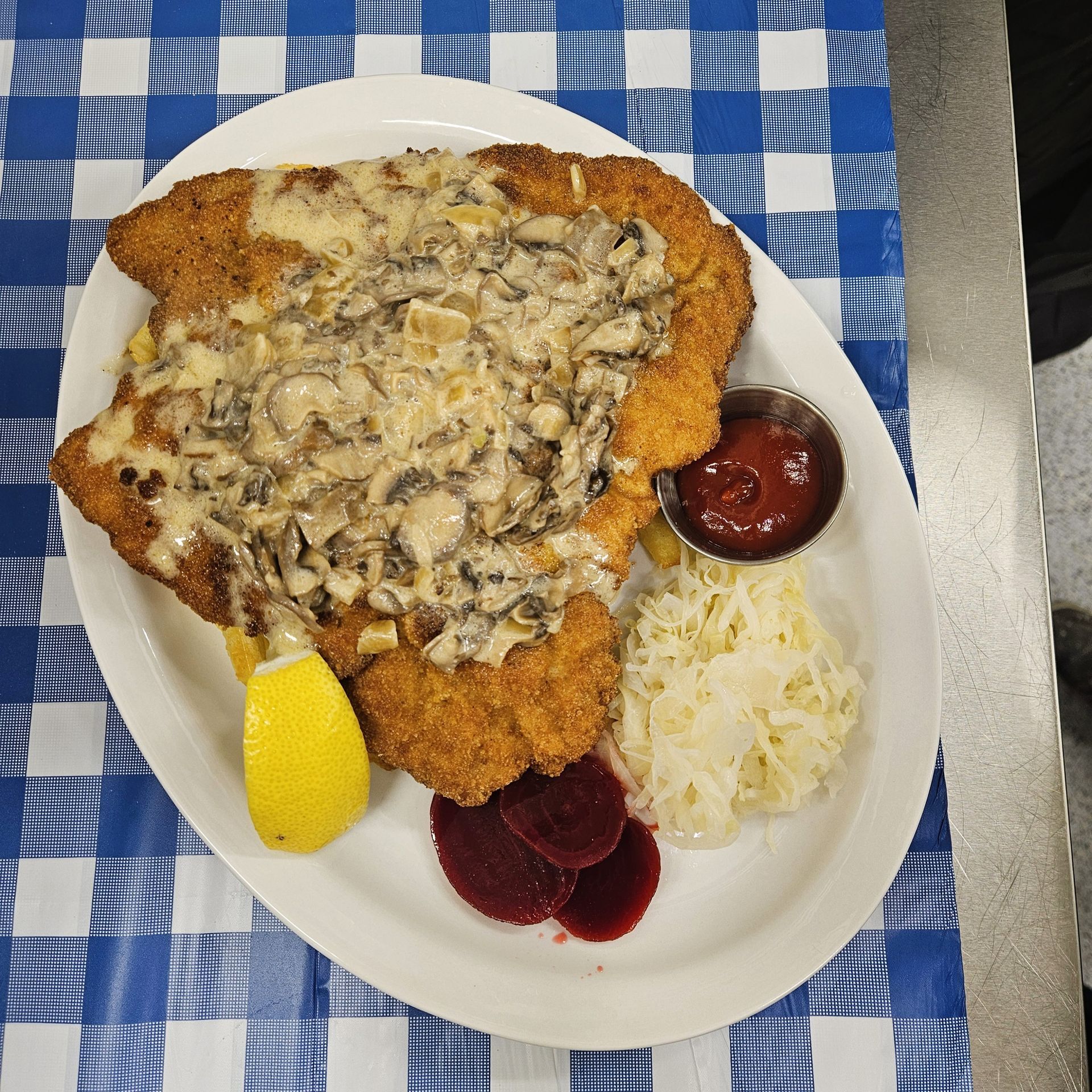 Breaded schnitzel with mushroom gravy, sauerkraut, beets, ketchup, and lemon on a white plate.