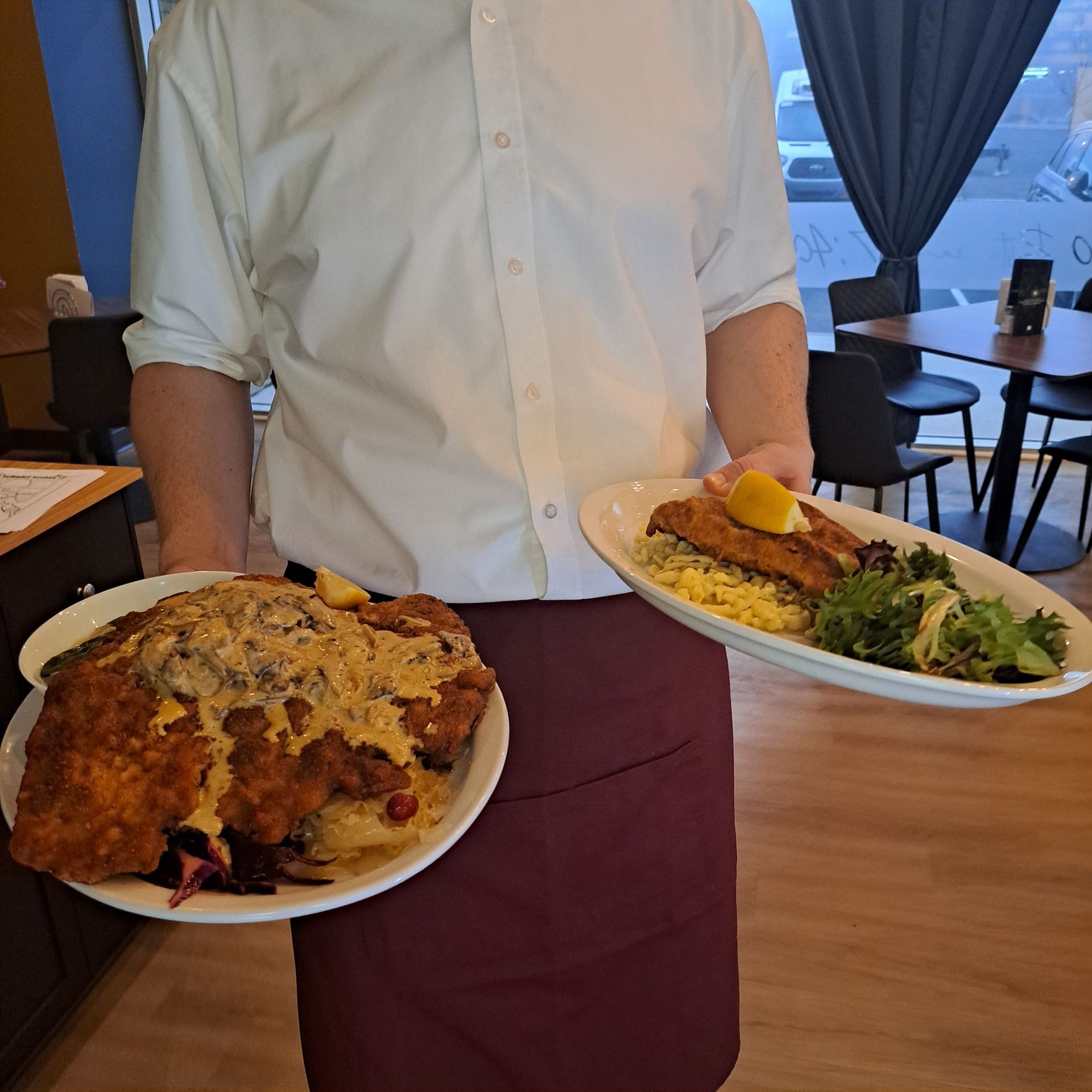 Waiter holding two plates of food in a restaurant. One plate has a large entree, the other, a smaller one.