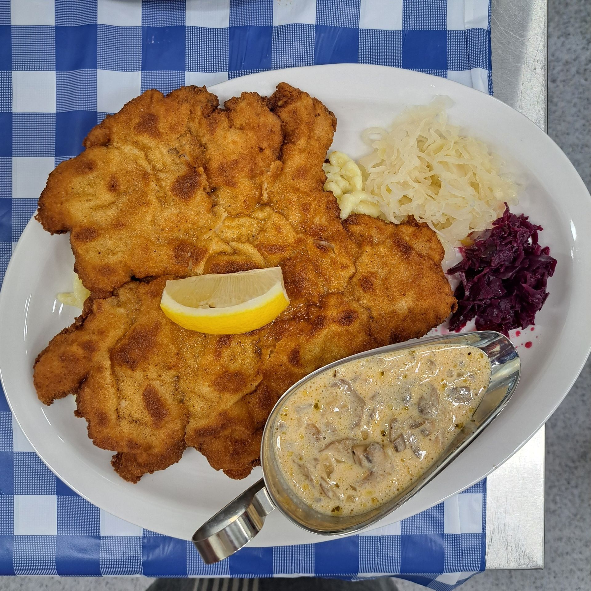 Breaded cutlets, sauerkraut, red cabbage, mushroom gravy, and a lemon wedge on a plate.