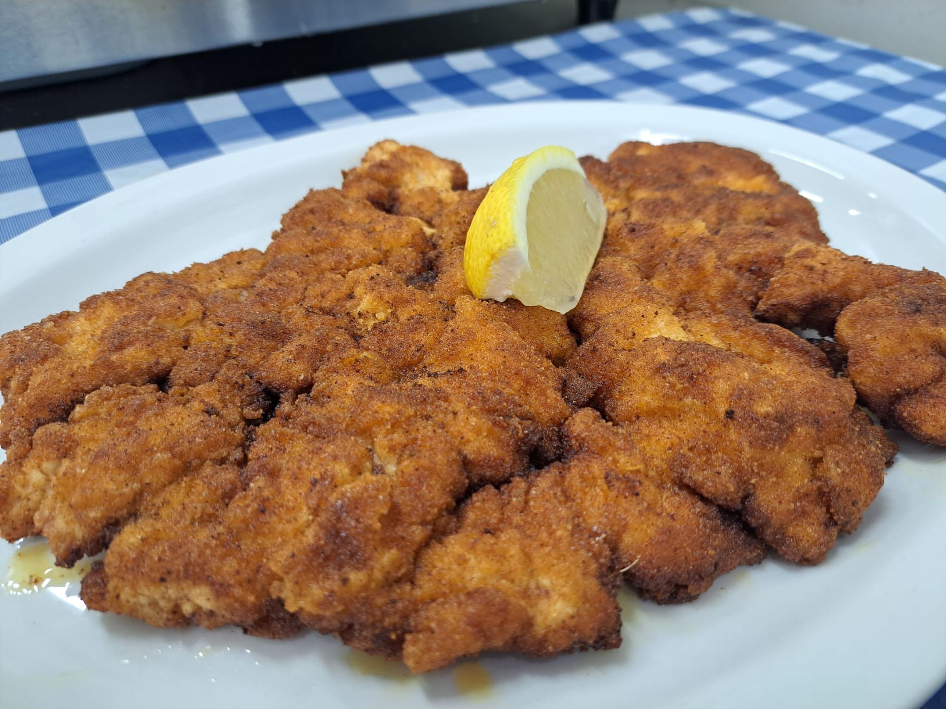 Golden-brown, breaded cutlets on a white plate, garnished with a lemon wedge, set on a blue and white checkered tablecloth.